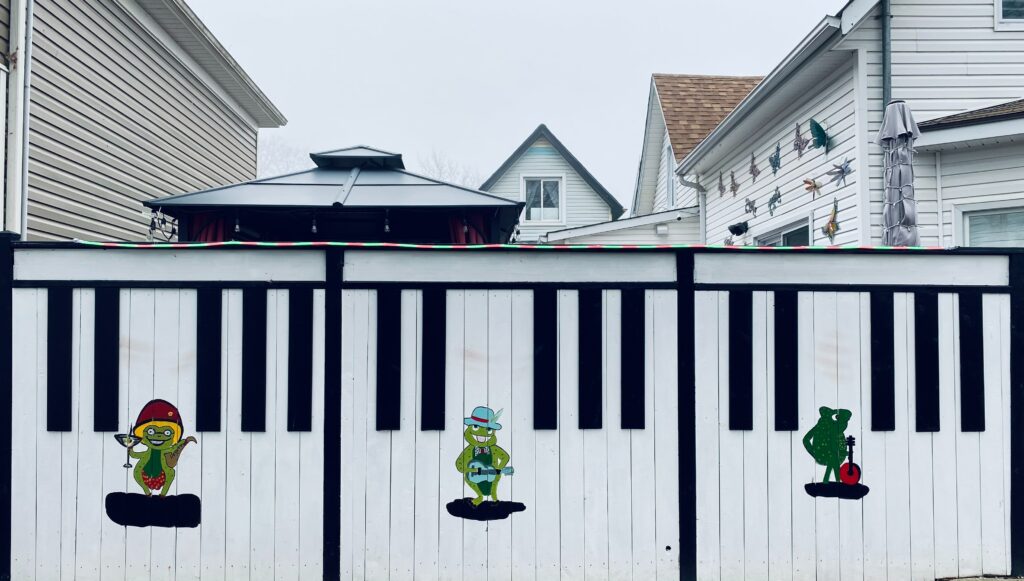 White fence with painted frog illustrations and black piano keys