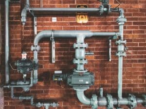 Industrial gas pipeline system with valves and meters installed against a brick wall, serviced by Dynamic Heating & Cooling in Hamilton, ON.